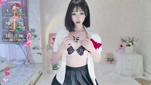 Media: A video of a slender Asian woman with short black hair, wearing a white blouse, black lace bra, and a black skirt, posing provocatively in a minimalist room with floral decorations and a pink poster in the background.