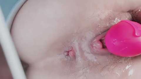 Media: Video of a close-up of a light-skinned person's genital area, with a pink vibrator inserted into the vagina. The skin is slightly moist and the surrounding pubic hair is sparse.