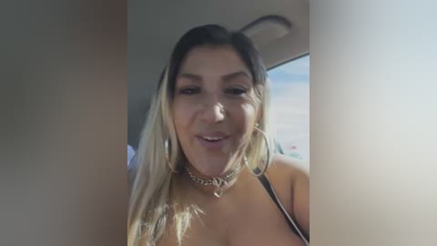 Media: Video of a smiling Latina woman with long, straight hair, wearing a black halter top, large hoop earrings, and a choker necklace. She has medium skin tone, dark eyes, and a friendly expression.