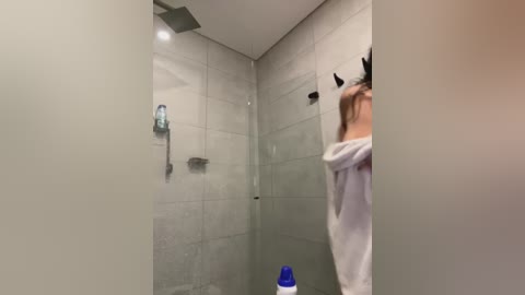 Media: Video of a modern, minimalist shower with light gray tiles, a blue shampoo bottle, and a person in a white robe.