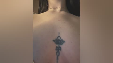 Video of a woman's upper back, showing a detailed black ink tattoo of a lantern with intricate designs, surrounded by a chain motif. She has light skin and wears a thin gold necklace.