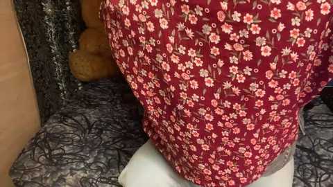 Media: Video of a maroon dress with a floral pattern featuring white and pink flowers, draped over a mannequin with a black and white lace skirt. Background includes a tan teddy bear and a dark floral fabric.