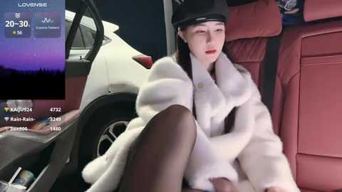 Media: Video of a young Asian woman in a white fur coat, black hat, and sheer black stockings, seated in the back of a white SUV at night, with a virtual overlay showing her stats.