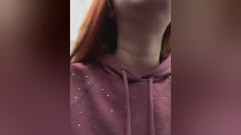 Media: A video of a person with light skin and long, straight red hair, wearing a pink hoodie with small white polka dots. The background is blurred, and the focus is on the neck and upper chest.