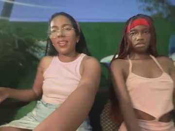 Video of two young Black women with medium-dark skin tones, wearing matching light pink sleeveless tops and denim shorts. One has red braids, the other straight hair, both smiling.