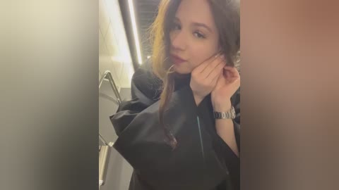 Media: Video of an Asian woman with long brown hair, wearing a black robe, adjusting her hair in a dimly lit bathroom.