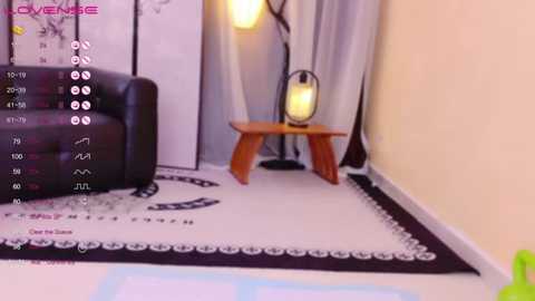 Video of a modern, minimalist living room with a black leather armchair, wooden side table, and a white lampshade; beige walls and a white and black patterned rug.