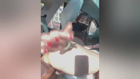 Media: A blurry video inside a car, showing a person with a mask and a black top, holding a phone, in daylight.