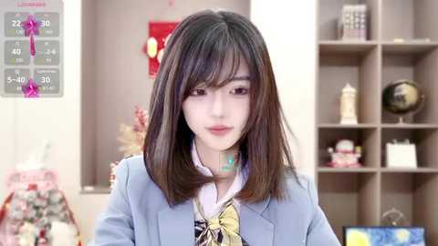 Media: A video of an Asian woman with straight, shoulder-length black hair in a light blue blazer, standing in a well-lit room with a pink calendar and bookshelf in the background.