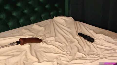 Media: A video showing a dark green, tufted headboard and a white bedspread with two screwdrivers: one brown with a wooden handle, the other black, lying on the bed.