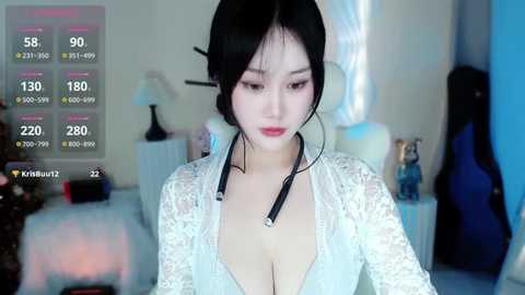 Media: Video of an East Asian woman with pale skin, black hair in a bun, wearing a revealing white lace dress, standing in a dimly lit room with musical instruments.