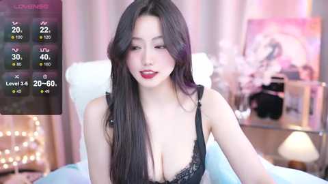 Media: Video of a young East Asian woman with long, dark hair and fair skin, wearing black lace lingerie, in a bedroom with a pink and white color scheme, featuring a bedside table with a lamp.