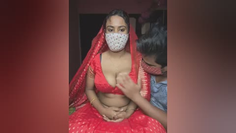 Media: Video of a pregnant Indian woman in a red sari with a patterned face mask, seated on a floor with a young child in a blue shirt and pink mask in the background.