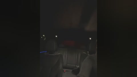 Media: A dimly lit video of a car's interior at night, showing the driver's seat with dark upholstery, a steering wheel, and a red brake light glowing faintly.