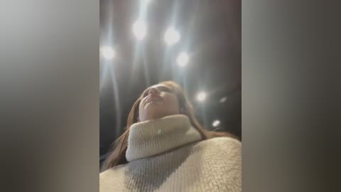 Video of a woman with long brown hair, wearing a cream-colored turtleneck sweater, looking up in awe at a bright, starry night sky with numerous stars and a few planets visible.