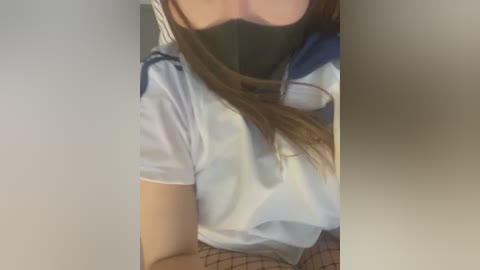 Media: Video of a person with long brown hair, wearing a light blue shirt, black face mask, and beige patterned shorts, partially visible.