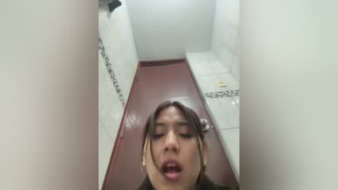 Media: A video of an Asian woman with short hair, lying face-down on a maroon bench in a tiled bathroom, eyes closed, mouth open, suggesting distress.