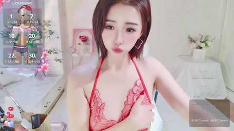 Media: Video of an East Asian woman with straight, shoulder-length brown hair, wearing red lace lingerie, standing in a bright, white room with floral decor, holding a phone, displaying a virtual reality game interface.