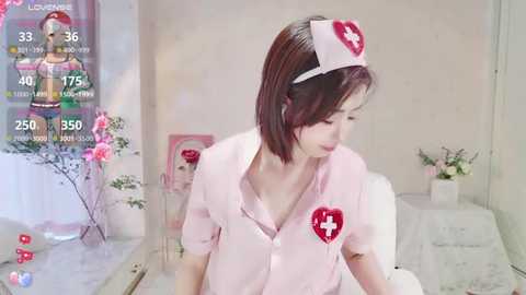 Media: A video of an Asian woman with short brown hair wearing a pink nurse outfit with a red cross, in a softly lit room.