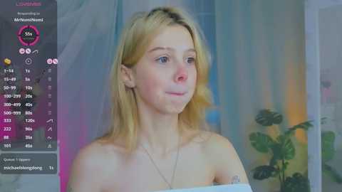 Media: Video of a young, blonde woman with fair skin, wearing a strapless top, in a room with a green plant, pink and blue lighting, and social media interface on the left.