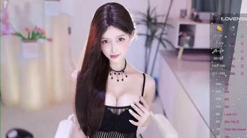 Media: Video of a slim, East Asian woman with long, straight black hair, wearing a black lace bra and necklace, sitting in a modern room with a potted plant and white furniture.