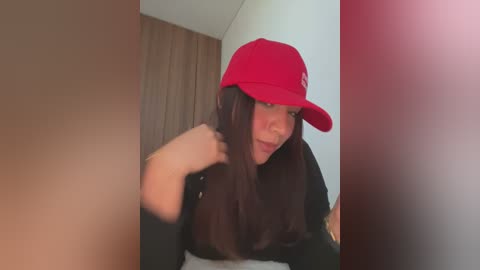 Media: A video of a young woman with long, dark hair, wearing a red baseball cap and a black top, adjusting her hair while indoors.