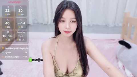 Media: A video of an East Asian woman with long black hair, wearing a revealing gold lace bra, sitting on a pink carpet in a room with a wooden crib and white curtains.