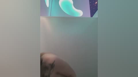 A blurry video of a nude, light-skinned person with blonde hair, partially obscured, standing in a dimly lit, minimalist room with a colorful, abstract wall art.