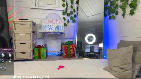 Media: A video of a bright, festive room with white walls, a \"FAMILY LINKS MISS YOU\" chalkboard, green potted plants, a white bed, and gift boxes, lit with blue and red lights.