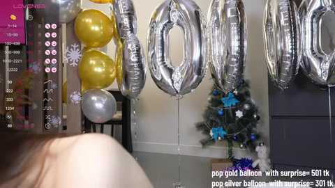 A video captures a close-up of a person's shoulder and neck, partially visible, holding silver balloons with \"600\" written on them. The background features a decorated Christmas tree.