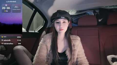 Media: Video of a young East Asian woman with long black hair and pale skin, wearing a black beanie, fur coat, and black top, seated in a car at night.