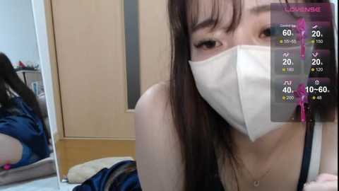 Video of an Asian woman with long black hair, wearing a white mask, black tank top, and pink earrings, indoors, showing a live stream overlay with health metrics.