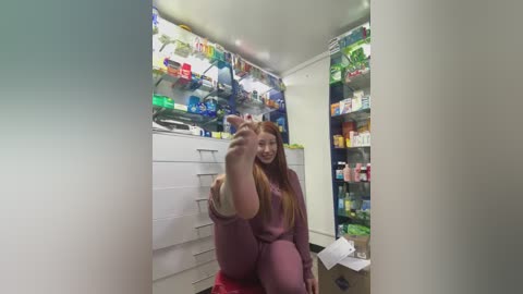 Media: Video of a young woman in a pink sweatshirt and red pants posing in a brightly lit, cartoon-themed convenience store, with shelves of colorful snacks and drinks in the background.