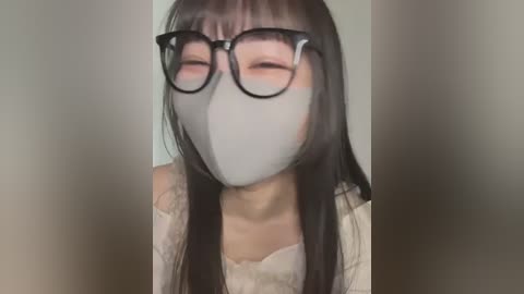 Media: Video of an East Asian woman with long black hair, wearing large black-framed glasses, white mask, and white lace top. The background is blurred and neutral.