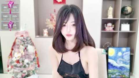 Media: Video of an East Asian woman with shoulder-length dark hair in a black lace camisole, sitting in a modern, minimalist room with a painting of Vincent van Gogh's \"Starry Night.\