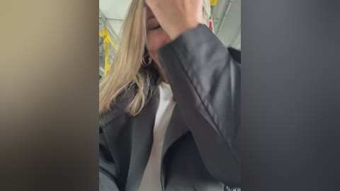 Media: A video showing a blonde woman in a dark suit, covering her face with her hand, taken from an overhead angle in a public setting with yellow seats visible.