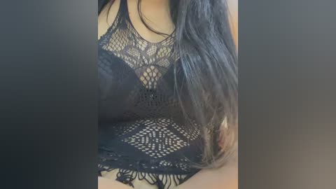 Media: A close-up video of a woman's chest, wearing a black lace bralette with intricate floral patterns. Her long, dark hair cascades over her shoulder. The background is blurred.