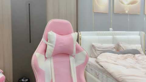 Media: Video of a pink and white gaming chair in a modern bedroom with a white tufted headboard bed, beige pillows, and minimalist decor.