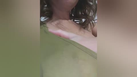 Media: Video of a woman's upper body, showing her bare shoulders and collarbone, with wavy, light brown hair, partially obscured by a green towel.