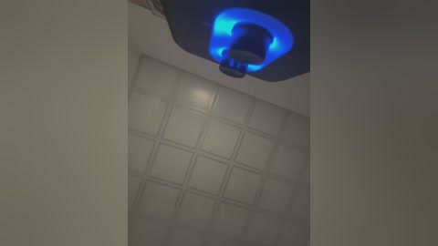 Media: Video of a ceiling fan with a bright blue light emitting from its base, set against a light beige textured ceiling and grid-patterned acoustic tiles.