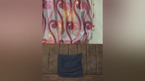 Media: Video of a brown upholstered bench with a dark blue pillow. Behind it, a pink and gray patterned curtain with string lights hangs against a beige wall. The image has a soft, warm glow.