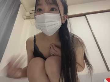 Media: Video of an East Asian woman with long black hair, wearing a white mask and black lingerie, seated on a bed in a dimly lit room with white walls and a window.