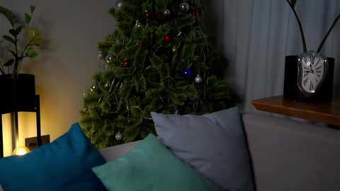 Media: Video of a cozy living room with a lit Christmas tree, blue and teal cushions, a wooden side table, and a black clock.