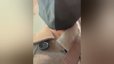 Media: A video of a person's torso wearing a beige trench coat with black buttons and a black face mask, focusing on the chest area and upper torso.