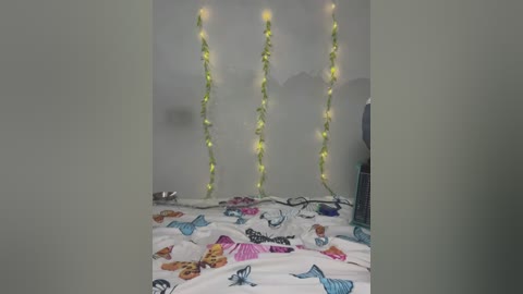 Media: A video of a misty bedroom with three glowing fairy lights, a white bedspread adorned with colorful butterflies, and a faint silhouette of a person in the background.