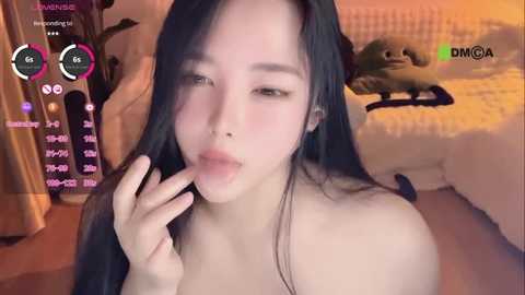 Media: Video of a young Asian woman with long black hair, light skin, and full lips, licking her fingers, in a cozy bedroom with a plush bed and toys.