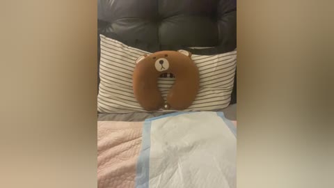 Video of a plush brown bear with a white snout on a striped pillow, lying on a bed with a blue blanket and pink quilted blanket.