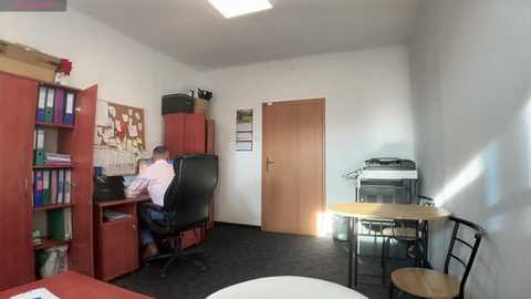 Media: A video of a small, well-lit office with a wooden desk, black chair, filing cabinet, bookshelf, white walls, and natural light from a skylight.