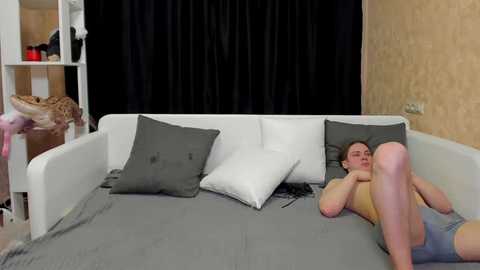 Media: A video of a woman in gray underwear lying on a gray bed with white pillows, black curtains, and beige wallpaper.