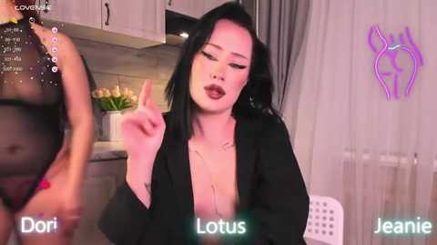 Media: Video of a young Asian woman with long black hair, wearing a black open robe, gesturing with her hand in a modern kitchen.